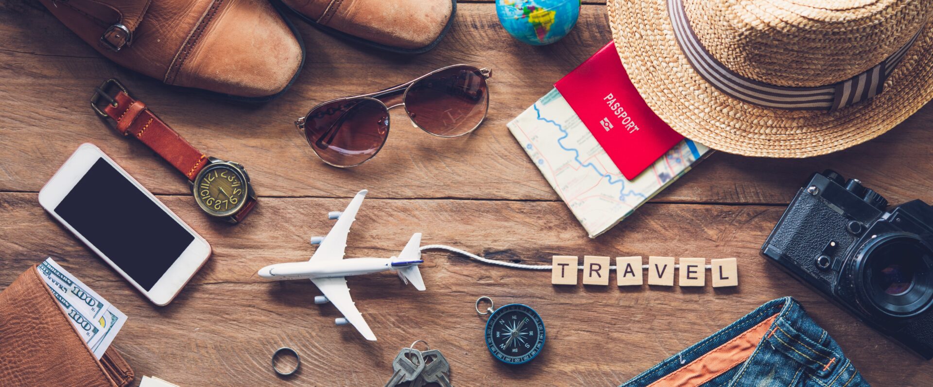 Essentials for your travel journey: passport, watch , cell phone, sunglasses, camera, hat, wallet with money, shoes, a toy airplane pulling the letters T R A V E L